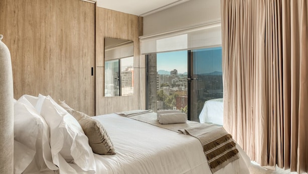 Une chambre d’hôtel moderne dotée d’un grand lit, d’une vue sur la ville et d’une porte-fenêtre coulissante.