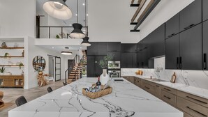 Une cuisine moderne dotée d’un grand îlot central, de meubles de couleur sombre et d’un plan de travail en marbre.