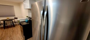 Una cucina con un frigorifero in acciaio inox, un piccolo tavolo con sedie e una finestra con persiane.