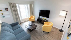 Una sala de estar con un sofá, dos sillones, una mesa de centro, un televisor y una lámpara.