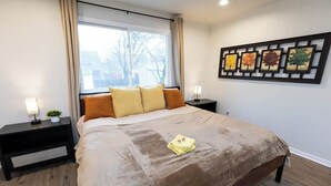 Un dormitorio con una cama grande, dos mesitas de noche, una ventana con cortinas y una obra de arte colgada en la pared.