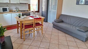 Cocina compacta con zona de comedor, un sofá gris y una planta en maceta.