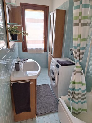 A compact bathroom with a sink, a washing machine, a mirror, and a shower curtain.