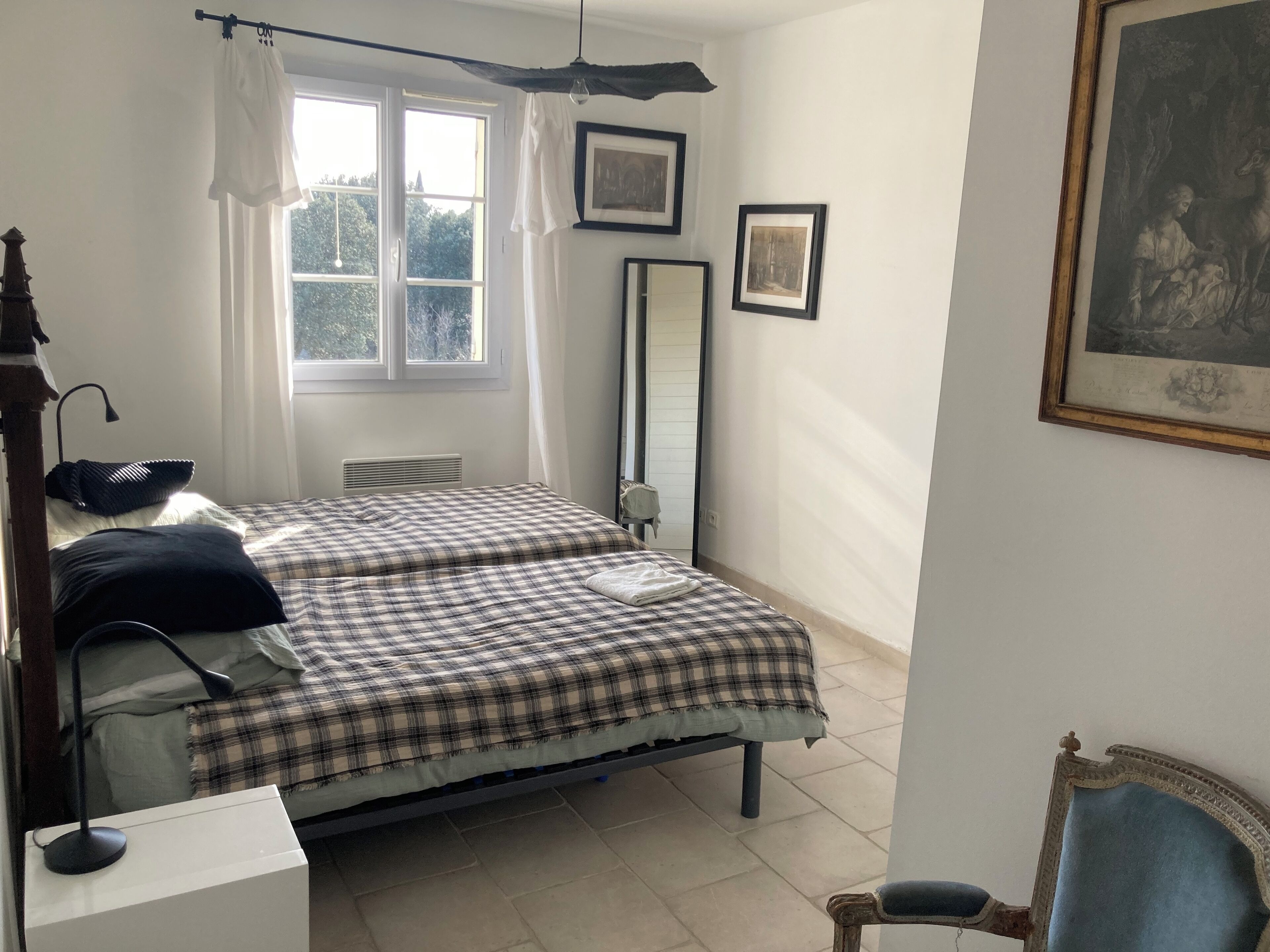 A bedroom with two beds, a desk, a chair, a window with curtains, and framed pictures on the wall.