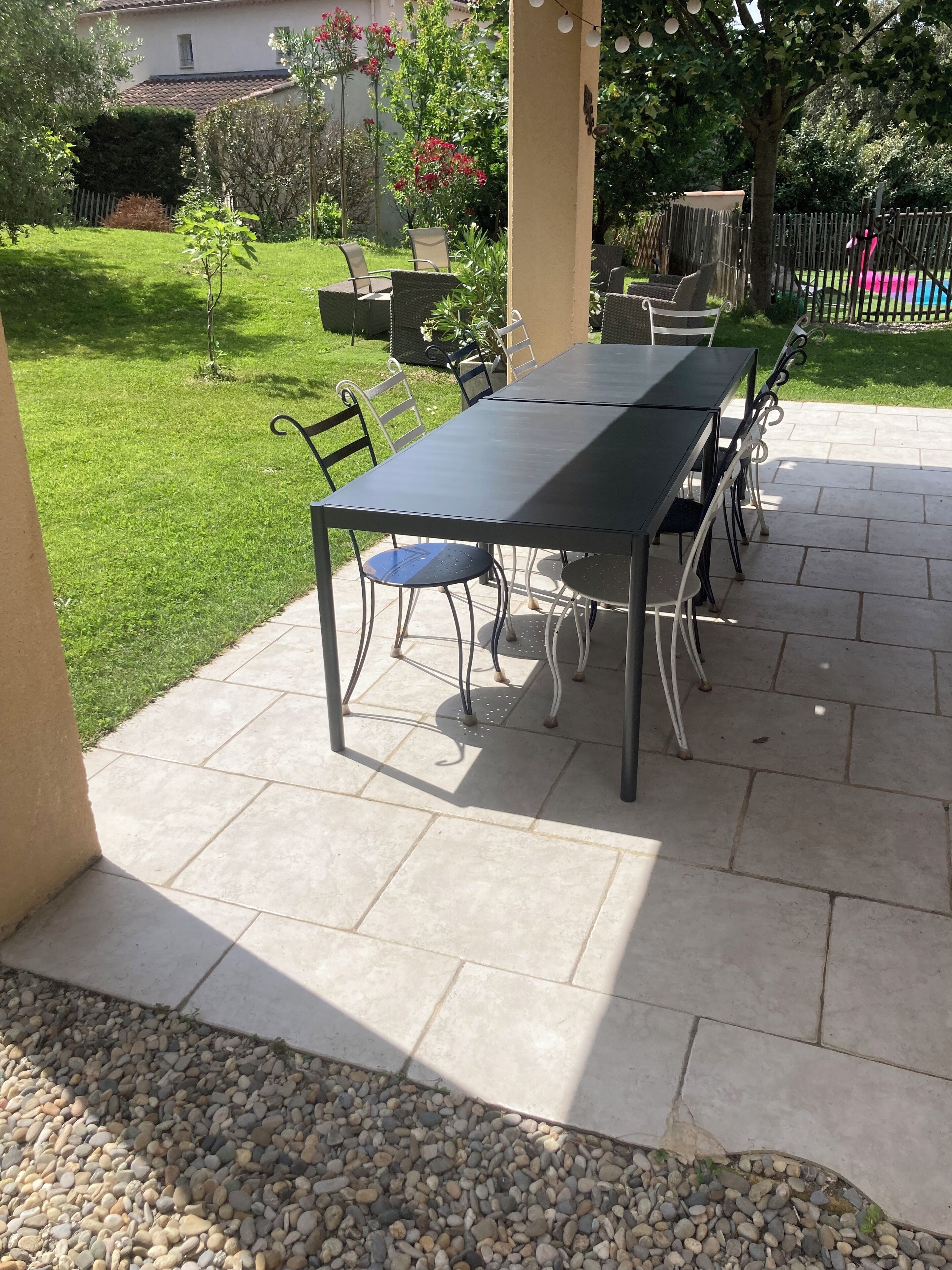 A patio with a table and chairs, surrounded by a garden and a fence.