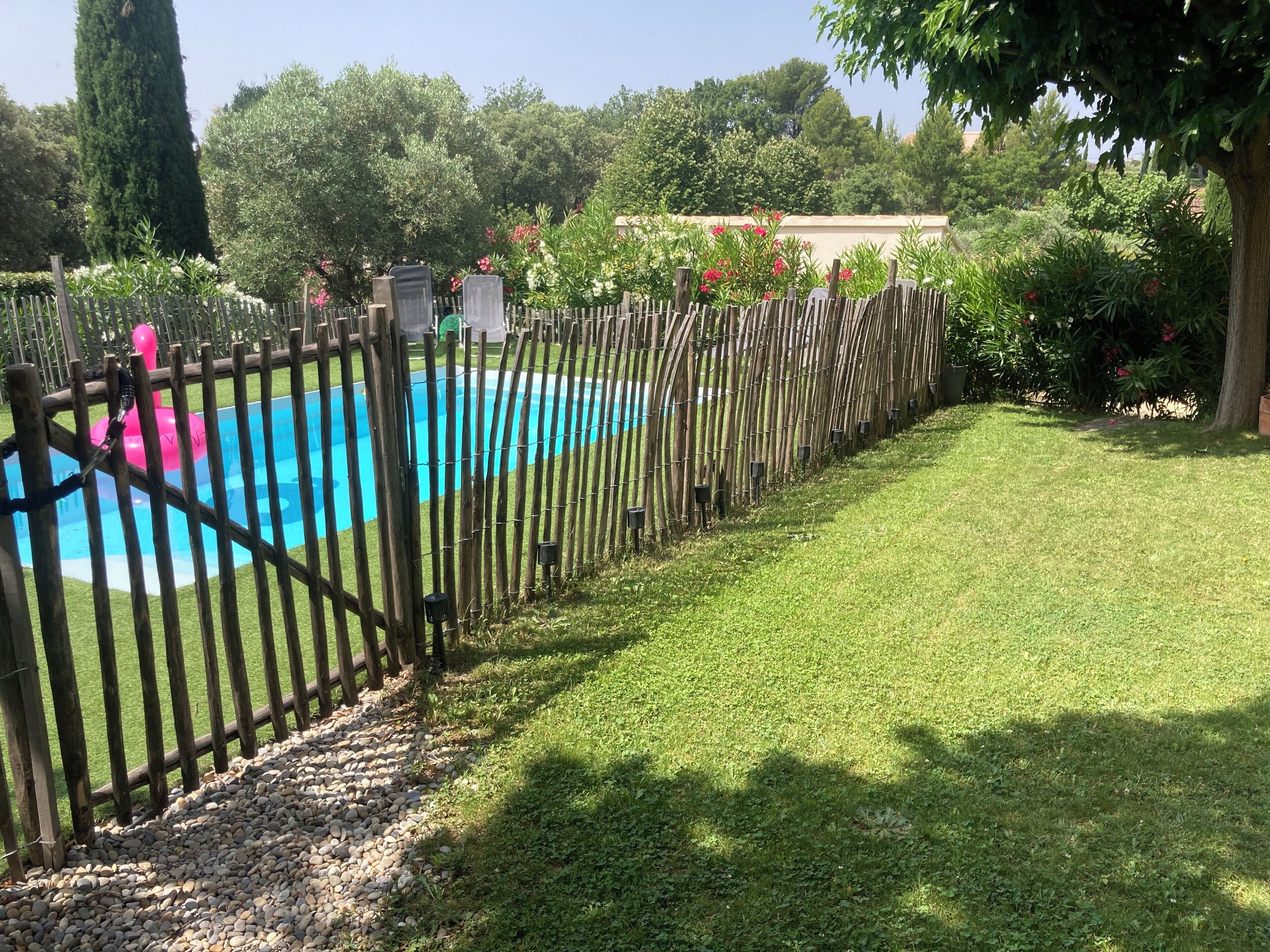 A swimming pool surrounded by a wooden fence, with a grassy area in the foreground and trees in the background.