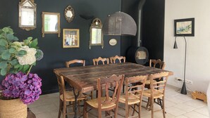 A dining area with a wooden table and chairs, a black wall with mirrors and a fireplace, and a potted plant with purple flowers. - Charming house in Provence, quiet and pleasant (Aubignan)