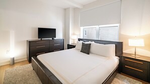 Una camera d'albergo moderna con un letto grande, una TV a schermo piatto, un comodino con una lampada e una finestra con tende.
