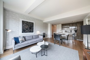 A modern living room with a grey sofa, a coffee table, and a dining area with chairs and a table.