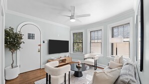 A living room with a flat-screen TV, two white armchairs, a grey sofa, a coffee table, and a ceiling fan. - Guest Favorite Newly Renovated 1BR Near Lakeview (Chicago)