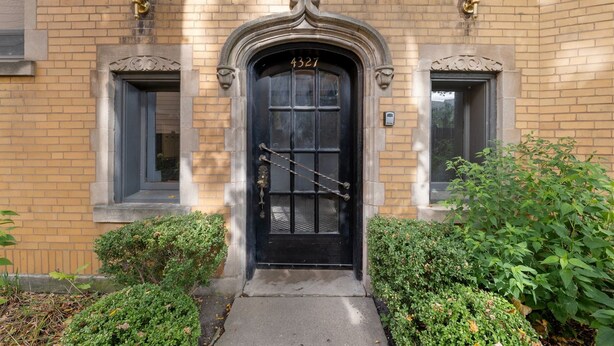 A black door with the number 4327, flanked by two windows with decorative brackets, set in a brick building with a small garden area in front. - Guest Favorite Newly Renovated 1BR Near Lakeview (Chicago)