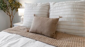 A neatly made bed with a beige blanket and pillows, a bedside lamp, and a small plant. - Guest Favorite Newly Renovated 1BR Near Lakeview (Chicago)