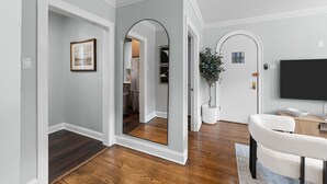 A modern living room with hardwood flooring, a white armchair, a flat-screen TV, and a potted plant. - Guest Favorite Newly Renovated 1BR Near Lakeview (Chicago)