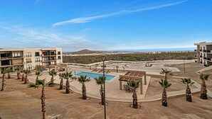 A resort with a pool, palm trees, and a view of distant hills. - OCEANVIEW 2 BR condo with AC, WiFi in enchanting Diamante area Cabo San Lucas! (Cabo San Lucas)
