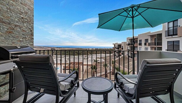 A balcony with a grill, two chairs, a table, and a large umbrella. - OCEANVIEW 2 BR condo with AC, WiFi in enchanting Diamante area Cabo San Lucas! (Cabo San Lucas)