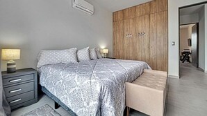 A modern bedroom with a large bed, bedside tables, a wardrobe, and an air conditioning unit. - OCEANVIEW 2 BR condo with AC, WiFi in enchanting Diamante area Cabo San Lucas! (Cabo San Lucas)