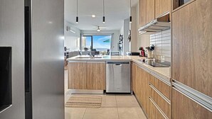A modern kitchen with wooden cabinets, a dishwasher, and pendant lighting. - OCEANVIEW 2 BR condo with AC, WiFi in enchanting Diamante area Cabo San Lucas! (Cabo San Lucas)