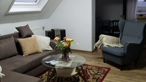 A living room with a brown sofa, a blue armchair, a glass coffee table with a vase of flowers, a patterned rug, and a skylight. - Vacation apartment Sonnenhaus Oppenhausen directly on the "Ehrbachklamm" dream loop (Boppard)