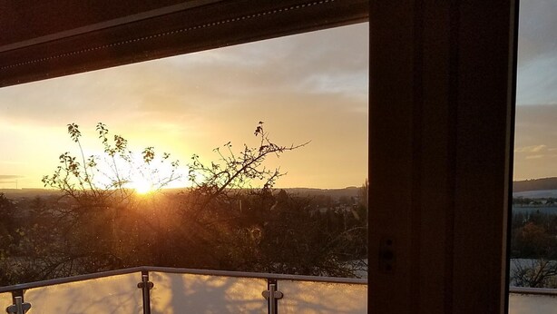 A balcony with a view of the sunset over a body of water, a table, and some potted plants. - Vacation apartment Sonnenhaus Oppenhausen directly on the "Ehrbachklamm" dream loop (Boppard)