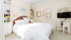 Un dormitorio con una cama grande, paredes blancas y un televisor sobre un mueble.