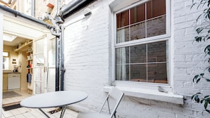 Fachada de ladrillo blanco con una ventana, una mesa pequeña y una silla.