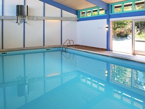 Ein Hallenbad mit einer Leiter, einer Uhr und einem Fenster mit Blick auf Grünflächen.