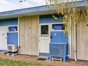 Ein Gebäude mit blau-weißer Fassade, einer Tür mit Fenster und einer kleinen blauen Struktur mit Lamellen.