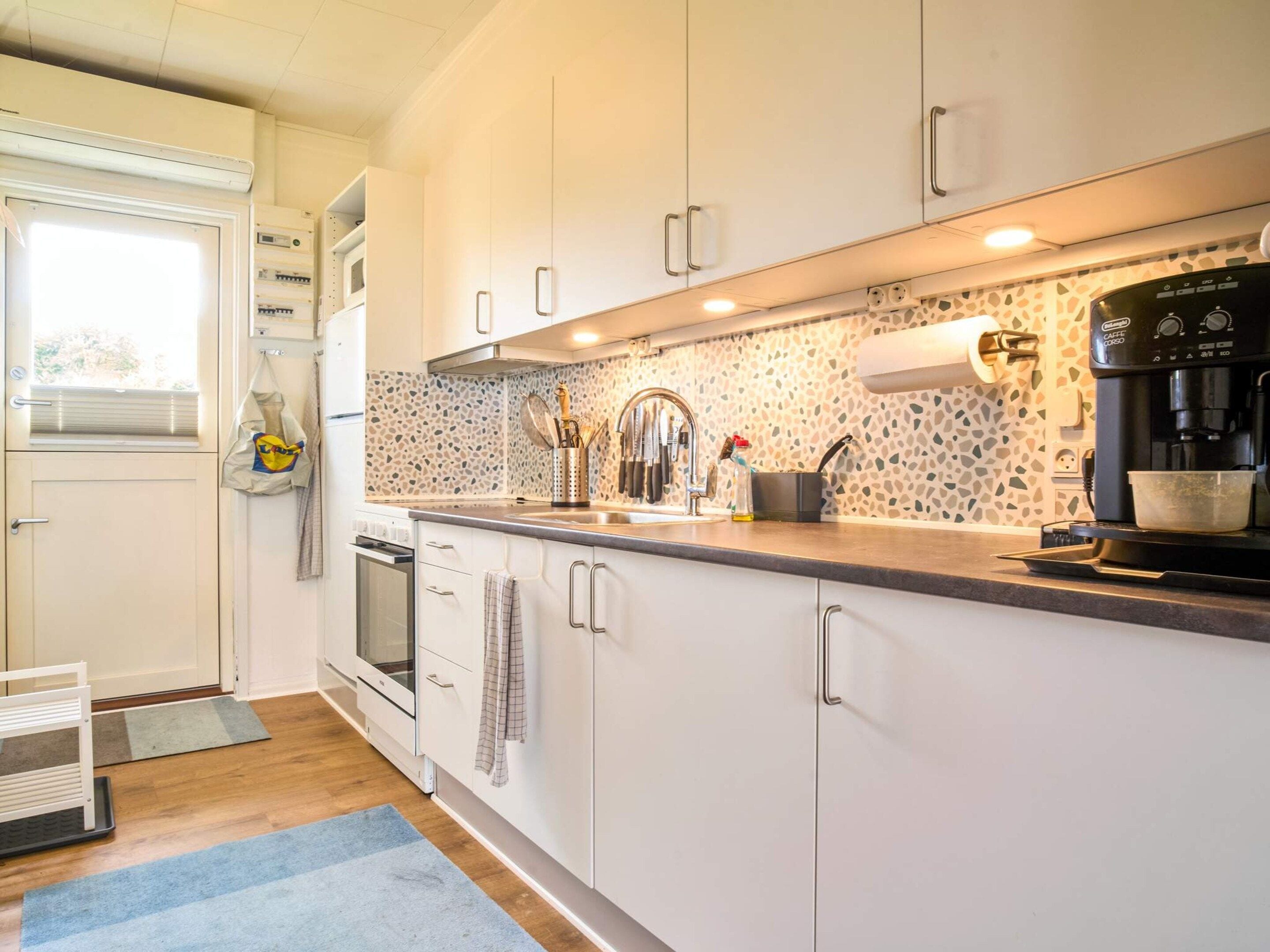 A modern kitchen with white cabinets, a built-in oven, a coffee maker, and a patterned backsplash.