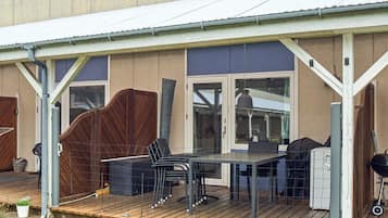 A covered outdoor patio with a table and chairs, a barbecue grill, and a fenced area.