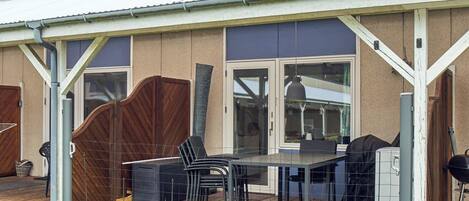 A covered outdoor patio with a table and chairs, a barbecue grill, and a fenced area.