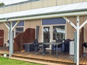 Un patio extérieur couvert, équipé d’une table et de chaises, d’un barbecue et d’un espace délimité par une clôture.