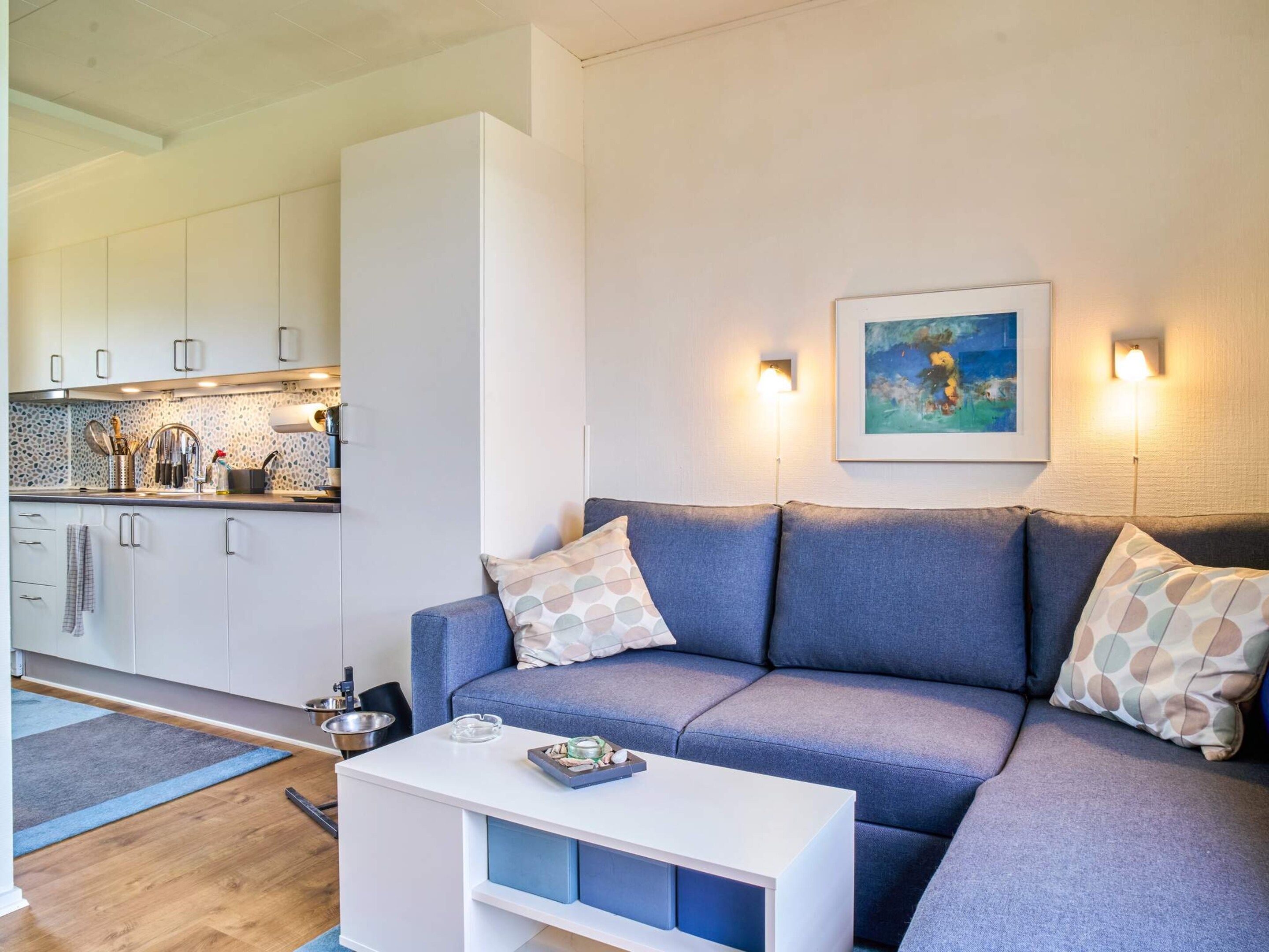 A modern living room with a sofa, a coffee table, and a kitchen area with cabinets and a countertop.