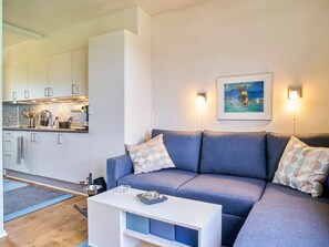 Ein modernes Wohnzimmer mit einer Couch, einem Couchtisch und einer Küchenzeile mit Schränken und einer Arbeitsplatte.