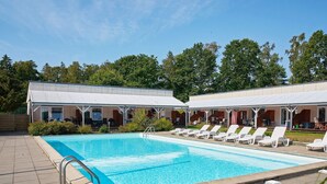 Piscina com espreguiçadeiras e áreas de estar com sombra.