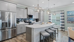 Una cocina moderna con electrodomésticos de acero inoxidable, una isla central con taburetes de bar e iluminación colgante.