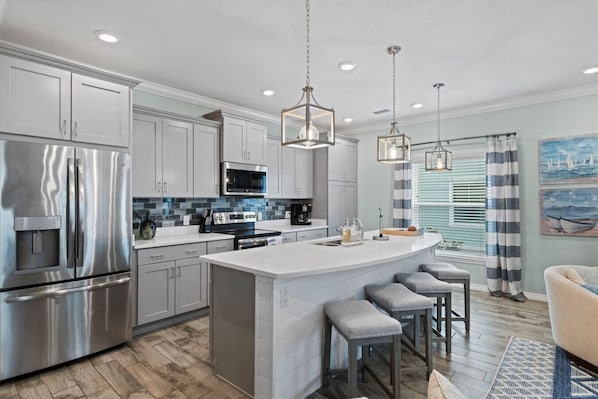 A modern kitchen with stainless steel appliances, a central island with bar stools, and pendant lighting.