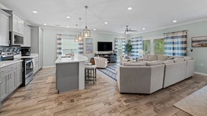 Una cocina moderna con una isla central, un área de comedor con un sofá y una sala de estar con televisor.
