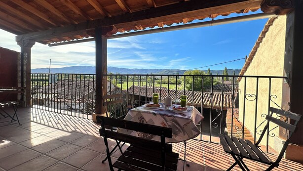 A covered outdoor seating area with a table set for two, overlooking a scenic landscape with mountains and a clear sky. - CASA RURAL EL POZO (San Bartolomé de Corneja)