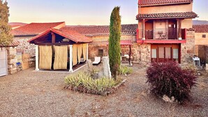 A traditional stone building with a red-tiled roof, a balcony, and a covered outdoor seating area. - CASA RURAL EL POZO (San Bartolomé de Corneja)