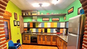 A kitchen with a tiled floor, a refrigerator, and a blue chair. - CASA RURAL EL POZO (San Bartolomé de Corneja)