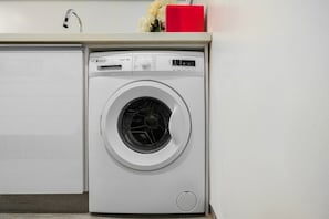 A front-loading washing machine with a control panel, a white wall, and a red object on top.