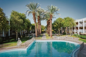 A swimming pool surrounded by palm trees and a building with multiple floors.