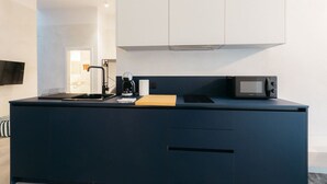 A compact kitchen with a dark countertop, a coffee maker, a microwave, and a wooden cutting board.