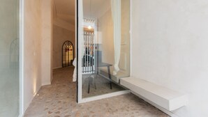 A hallway with a glass door leading to a room, a bench, and a small table.