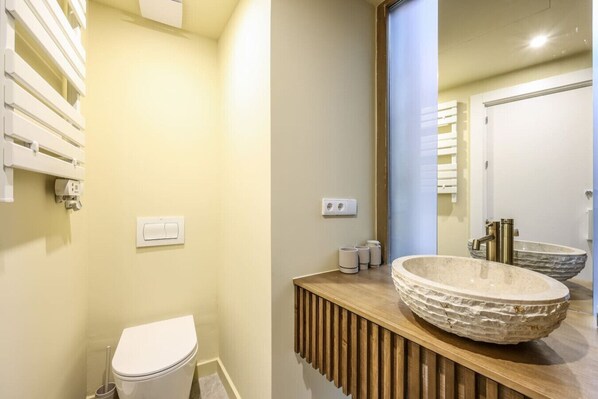 A modern bathroom with a white toilet, a wooden vanity with a large stone sink, and a mirror above the sink.