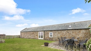 A stone building with a door and windows, a grassy yard, and outdoor furniture.