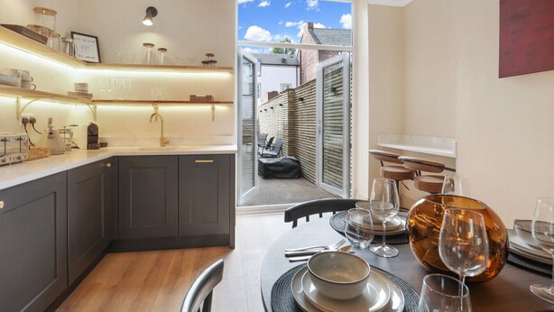 Una cocina moderna con horno integrado, un comedor con una mesa dispuesta para dos personas, y vistas al exterior a través de un ventanal.