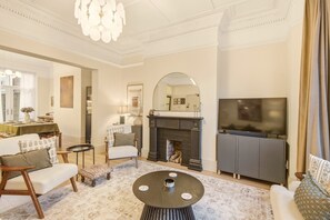 Un salon avec une cheminée, un canapé, un fauteuil, une table basse et un téléviseur.