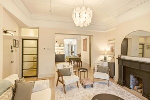 A spacious living room with a fireplace, a dining area with a table and chairs, and a kitchen in the background.