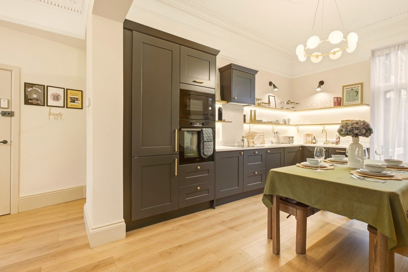 Une cuisine moderne avec des meubles de couleur sombre, un coin repas avec une table dressée pour deux personnes et un luminaire suspendu.